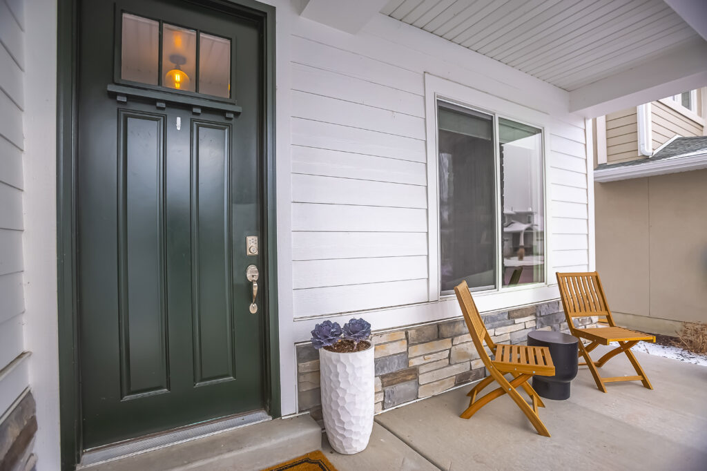 Front porch of home with white siding, dark green door, and wooden chairs